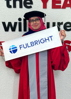 Risa Haridza in Ohio State graduation regalia holding a Fulbright sign