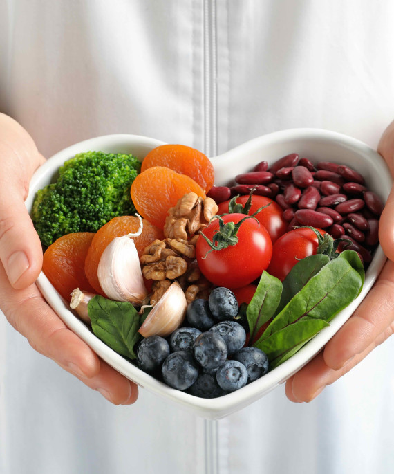 heart shaped bowl of healthy fruits and vegetables held by a person in white lab coat